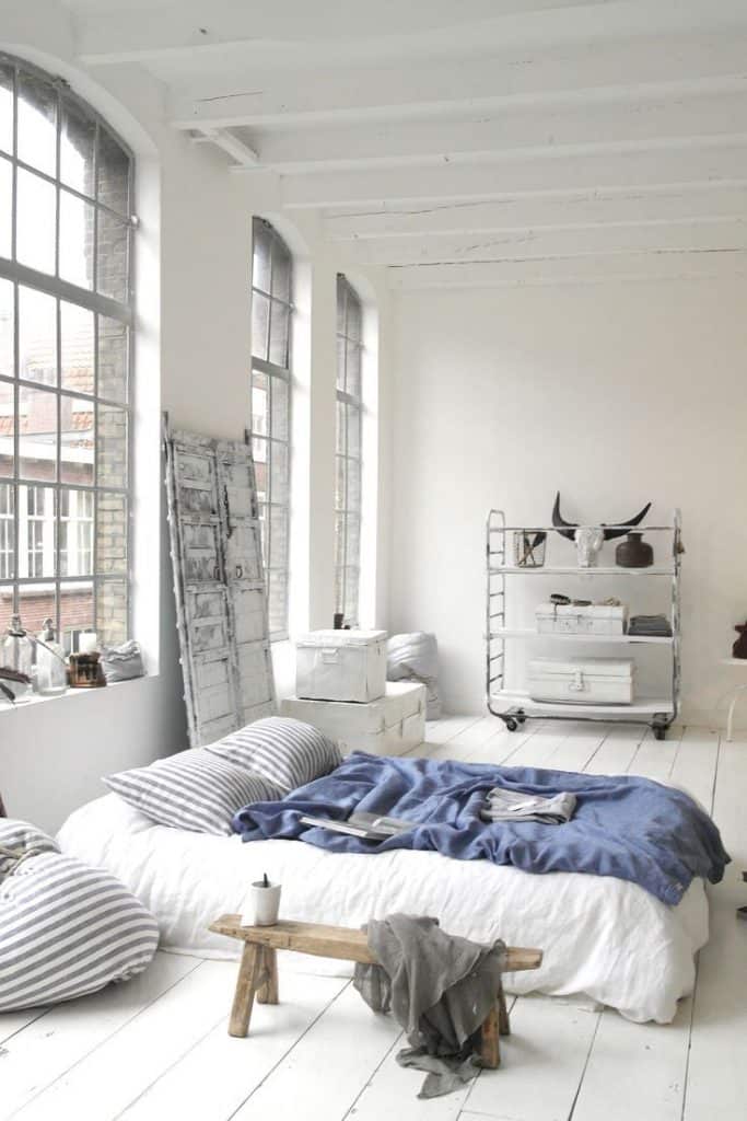 Dormitor alb cu ferestre inalte si largi cu pardosea de culoare alba si pat jos