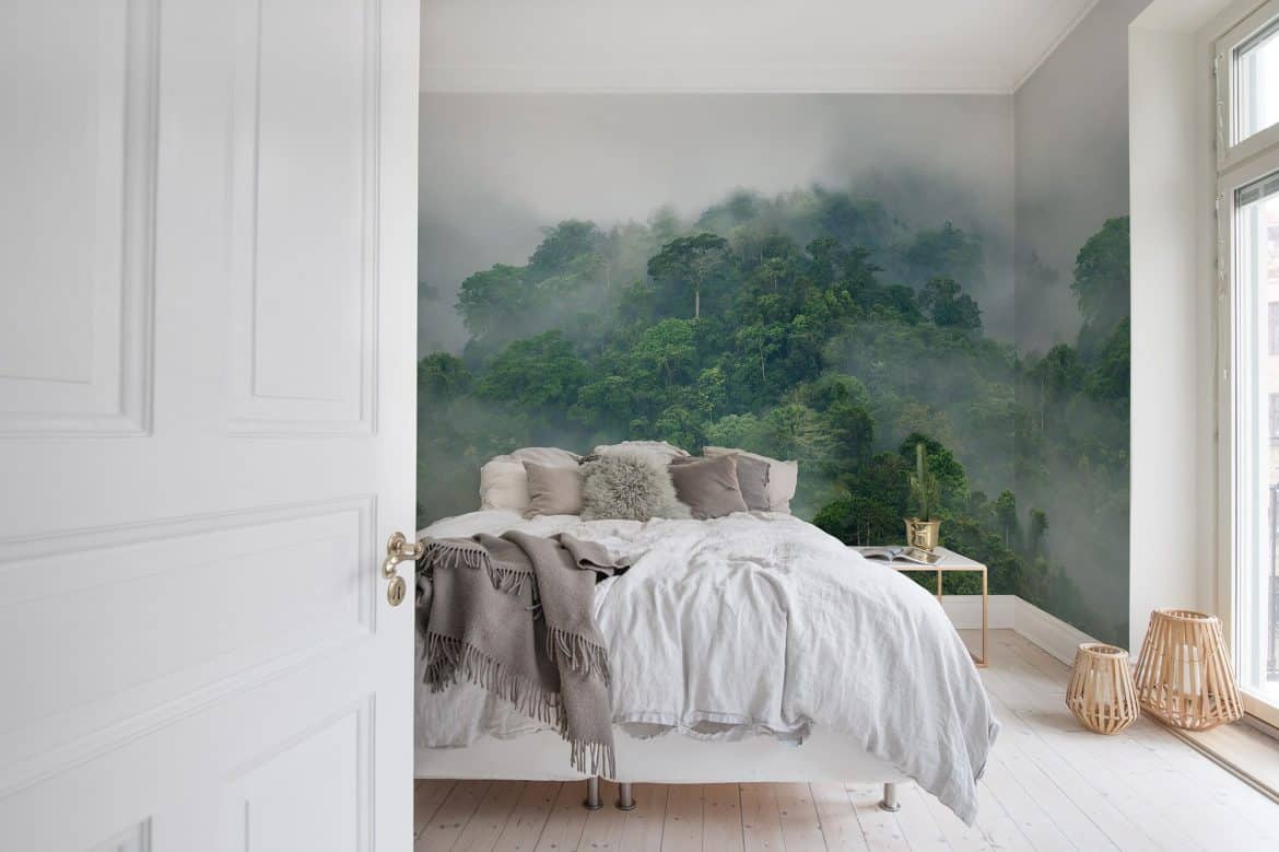 Dormitor cu pat alb si perne crem și fototapet pe doi pereti cu peisaj padure si ceata
