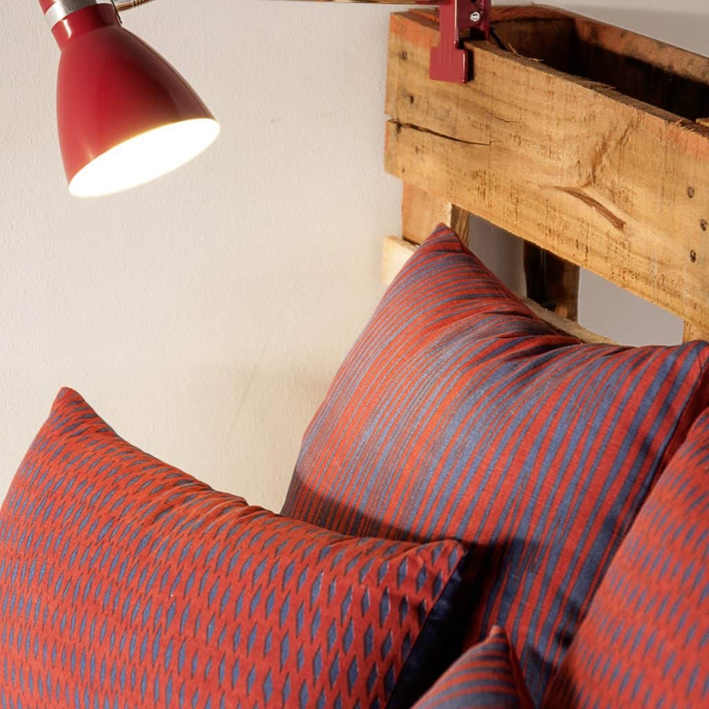 Lampa Study pe tablia unui pat pe care se afla mai multe perne colorate cu rosu si albastru