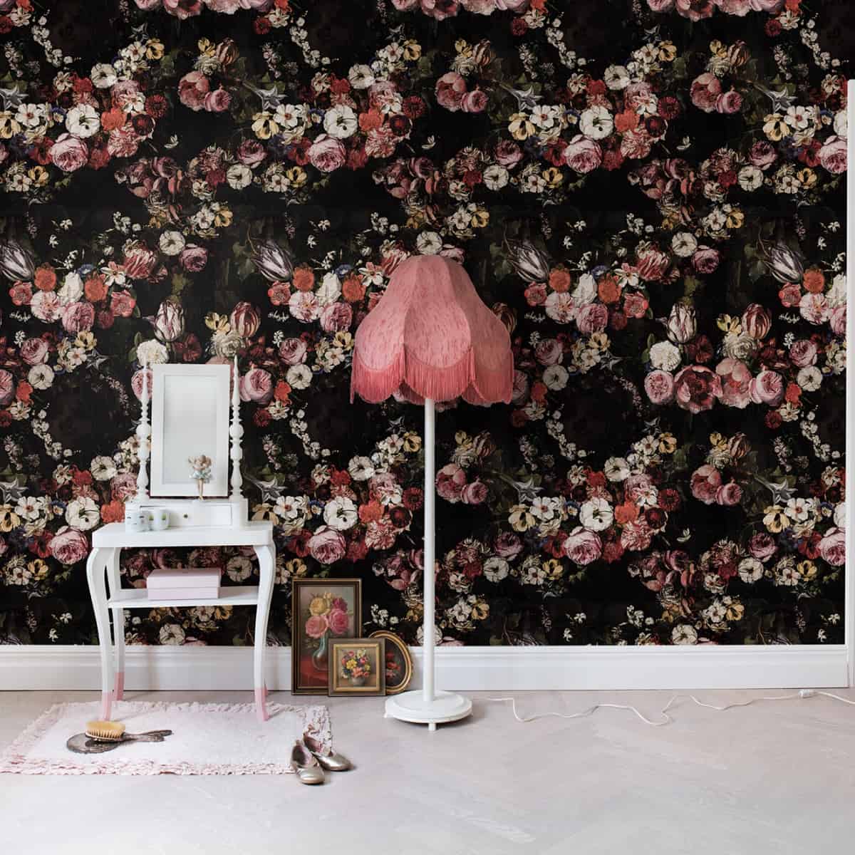 masuta decorativa cu oglinda si lampada rosu cu picior alb asezate langa un perete cu tapet 3D pe fundal negru cu flori colorate