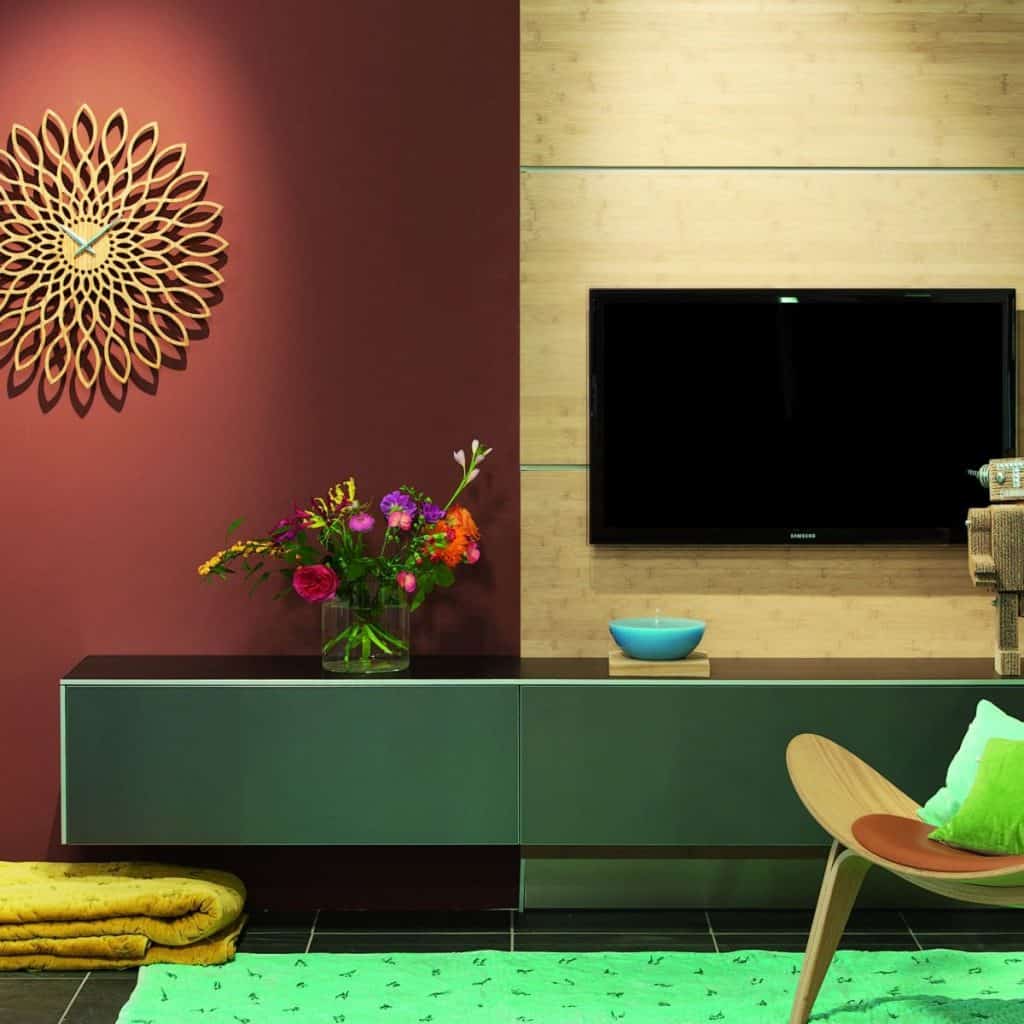Încăpere decorată cu un ceas de perete în formă de floarea soarelui, cu televizor suspendat pe perete și comodă neagra