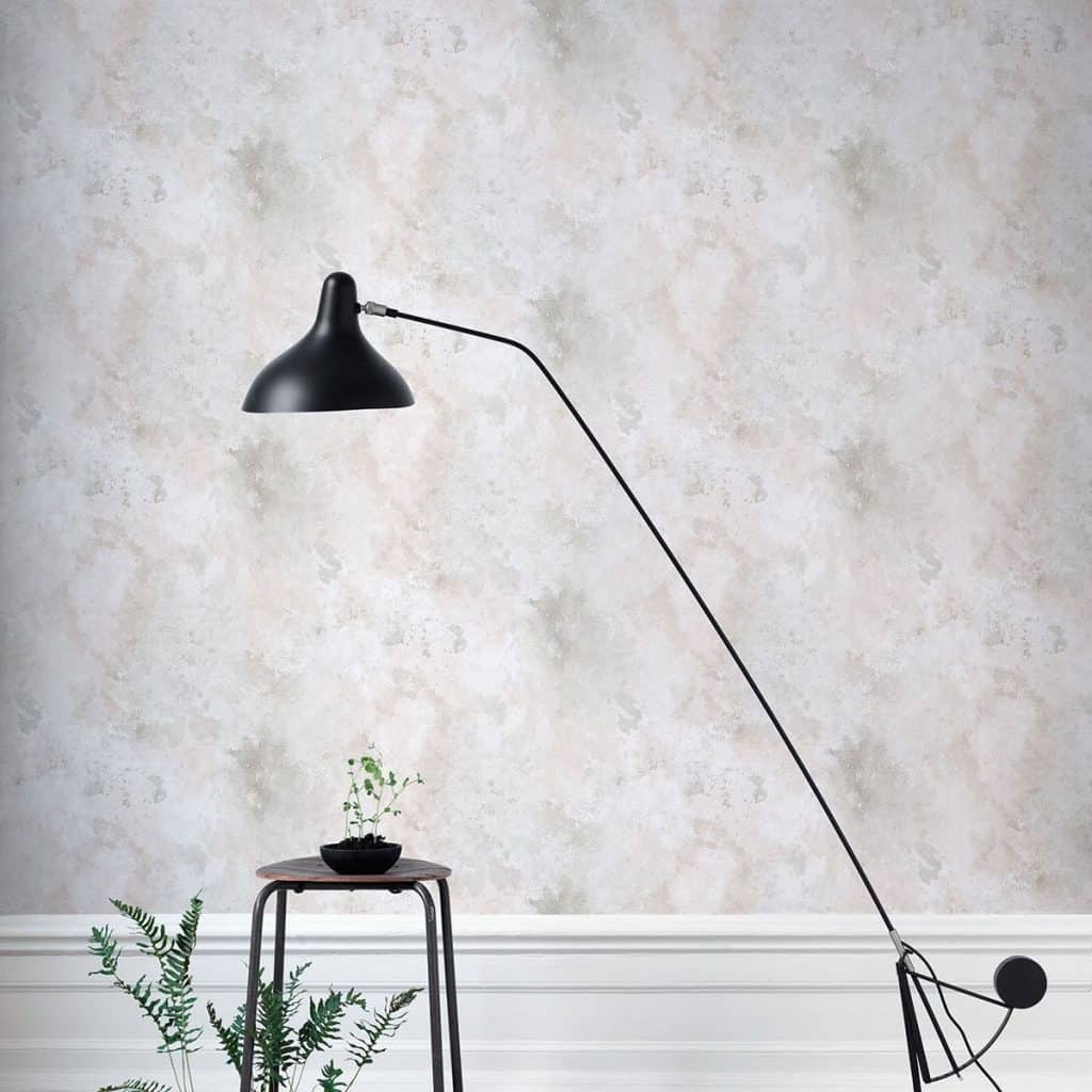 Perete decorat cu tapet deschis la culoare, în fața căruia se află o lampă și o măsuță cu o plantă decorativă