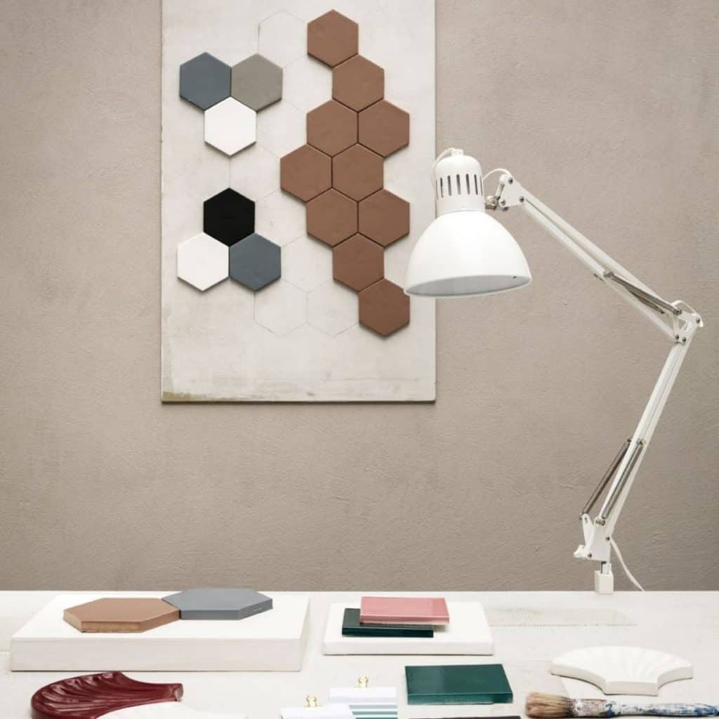 Modele de gresie hexagonala de diferite culori expuse pe un perete in fata caruia se afla o lampa alba