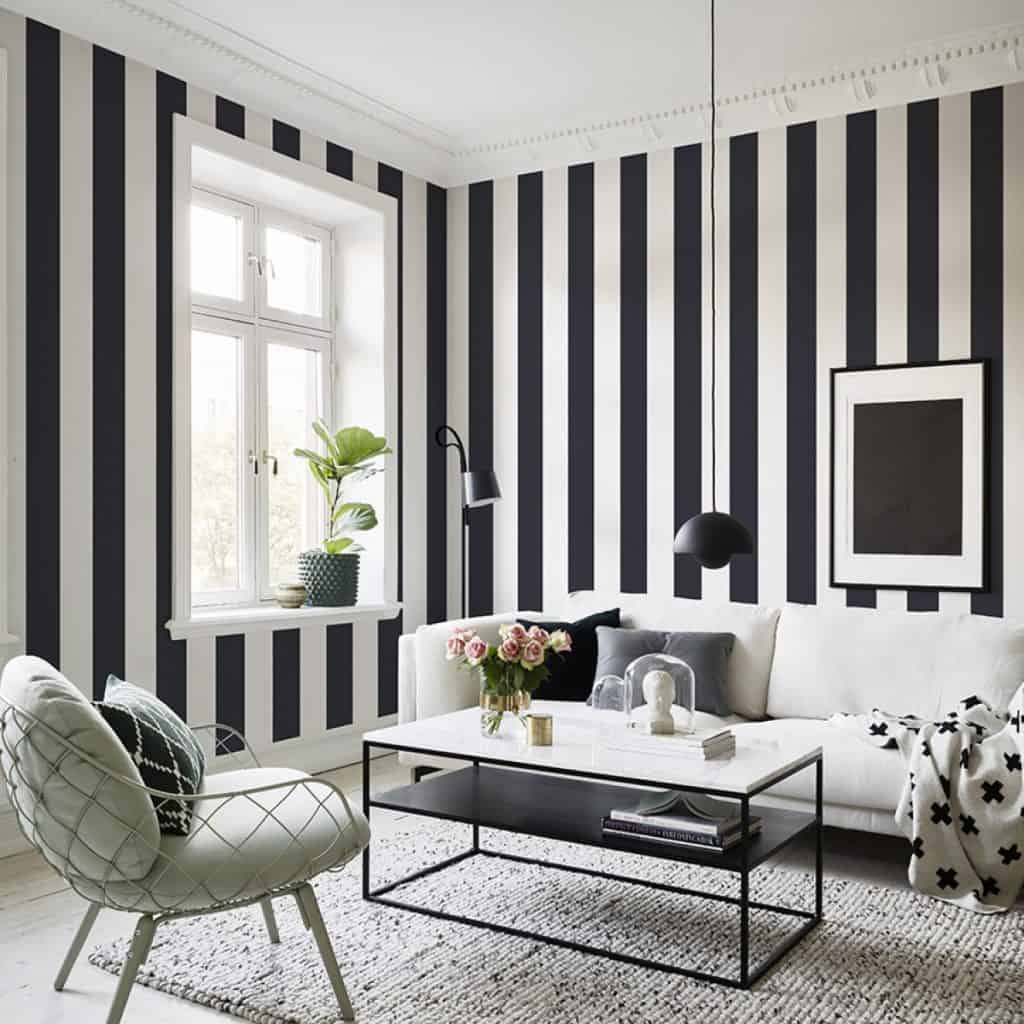 Living cu pereti cu tapet cu benzi verticale alb si negru, cu canapea, masuta de cafea, fotoliu, tablou, obiecte si flori decorative