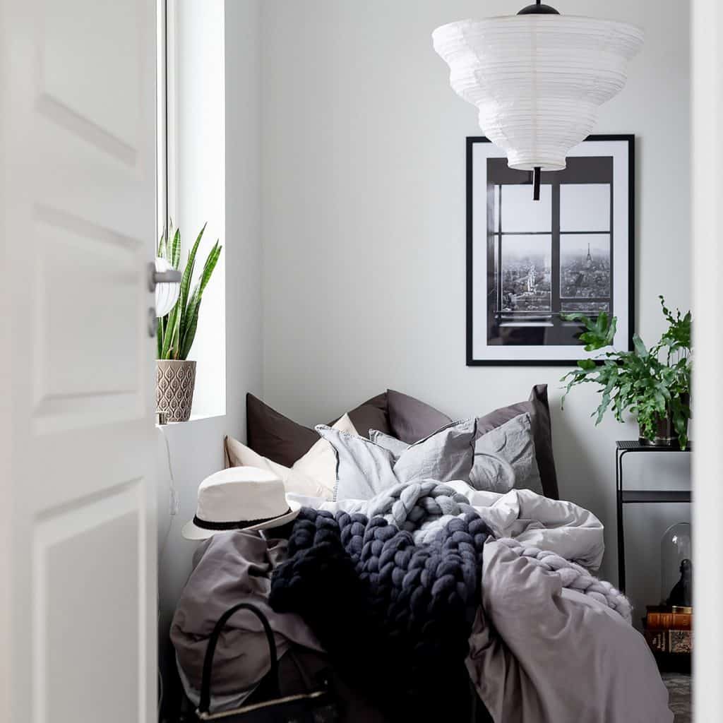Lampa suspendata alba intr-un dormitor cu pat, tablou si plante decorative