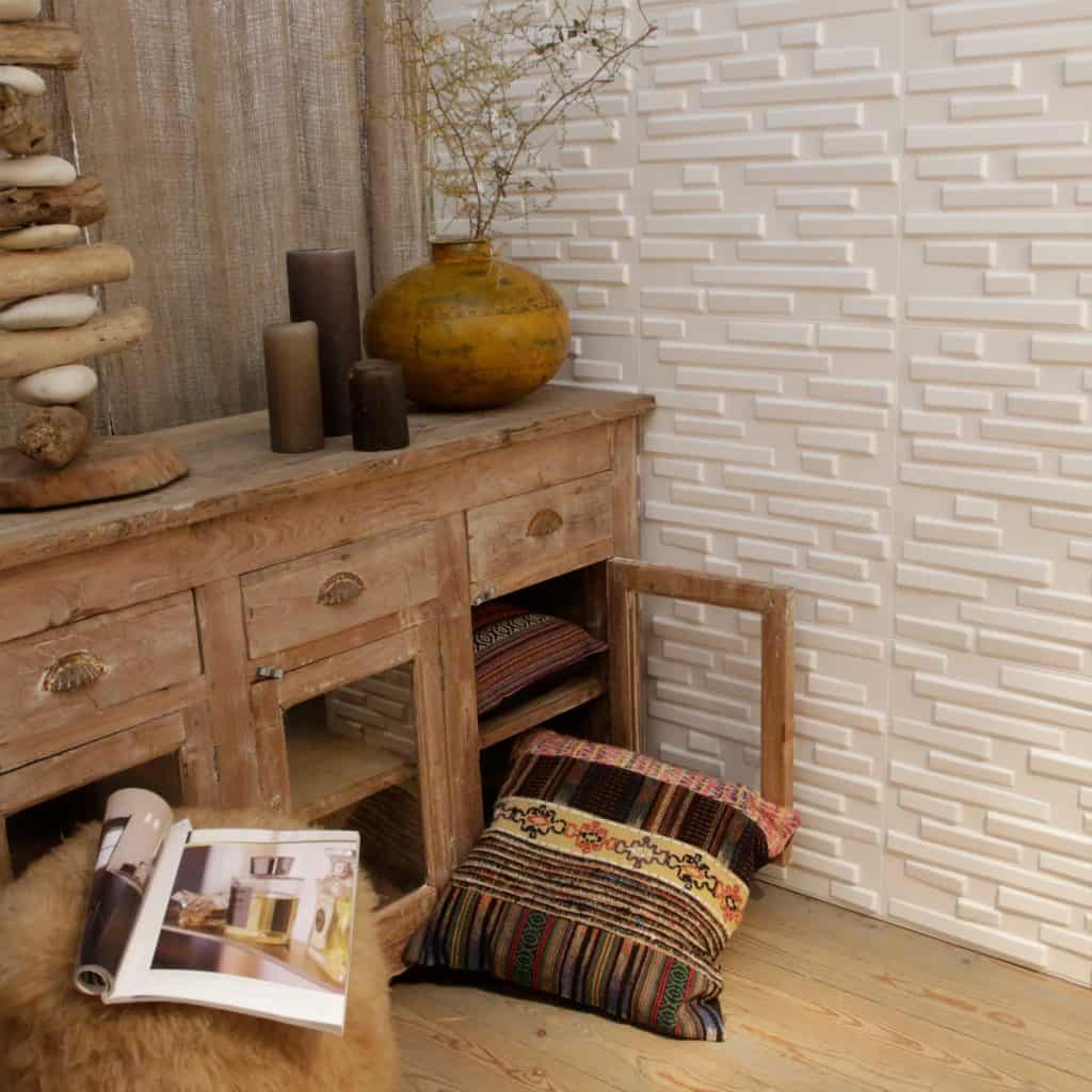 Perete cu profile decorative 3D albe langa o comoda din lemn cu lumanari, avs cu planta decorative si ornament din piatra