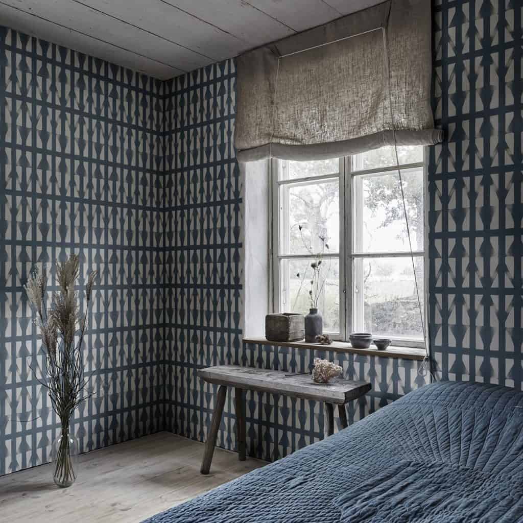 Camera cu tapet cu forme geometrice in nuante de gri, cu pat, masa de cafea si vas cu planta decorativa