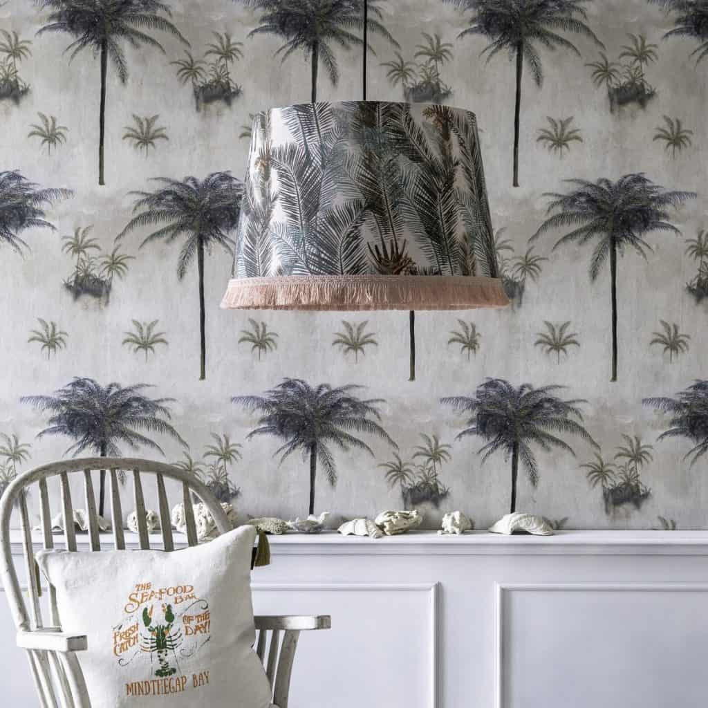 Lampa suspendata cu frunze de palmier într-o camera cu tapet cu palmieri, scaun si perna decorativa