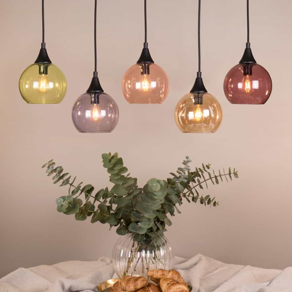 Lampa de tavan Palls cu cinci globuri din sticlă transparenta de nuante diferite, deasupra unei mese cu vas cu planta decorativa si croissante