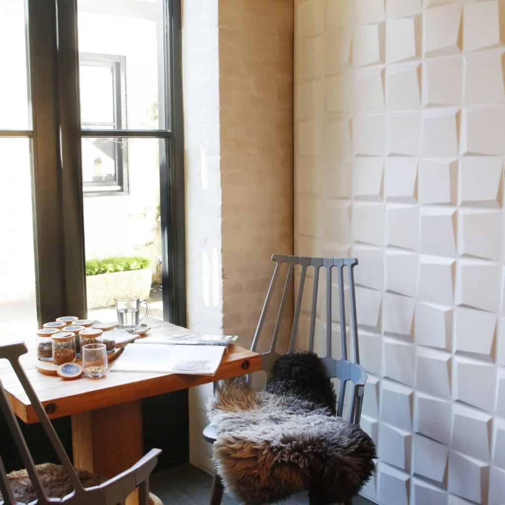Panouri decorative 3D Oberon intr-o incapere cu fereastra, masa cu pahare si o carte si doua scaune cu huse din blana