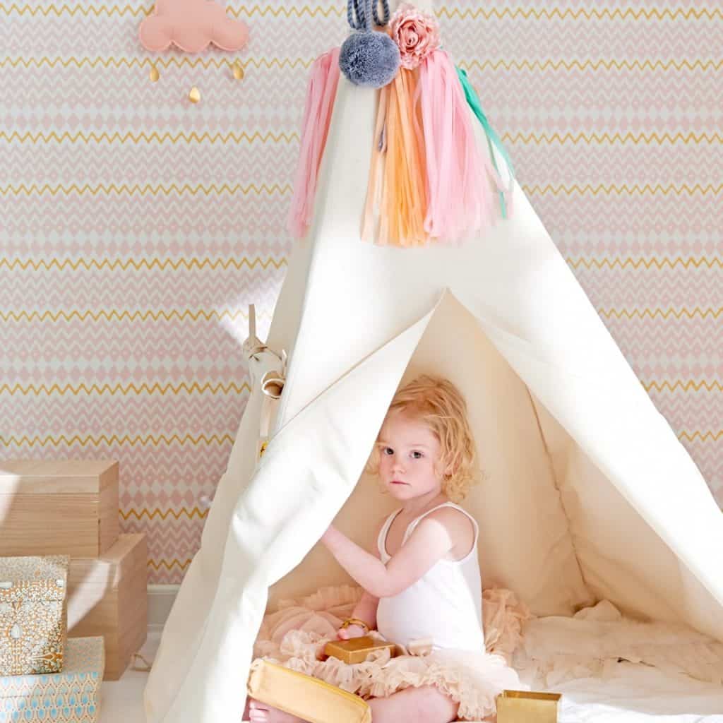 Tapet Tomoko in camera cu un cort in care se afla o fetita blonda, langa care se afla mai multe cutii colorate