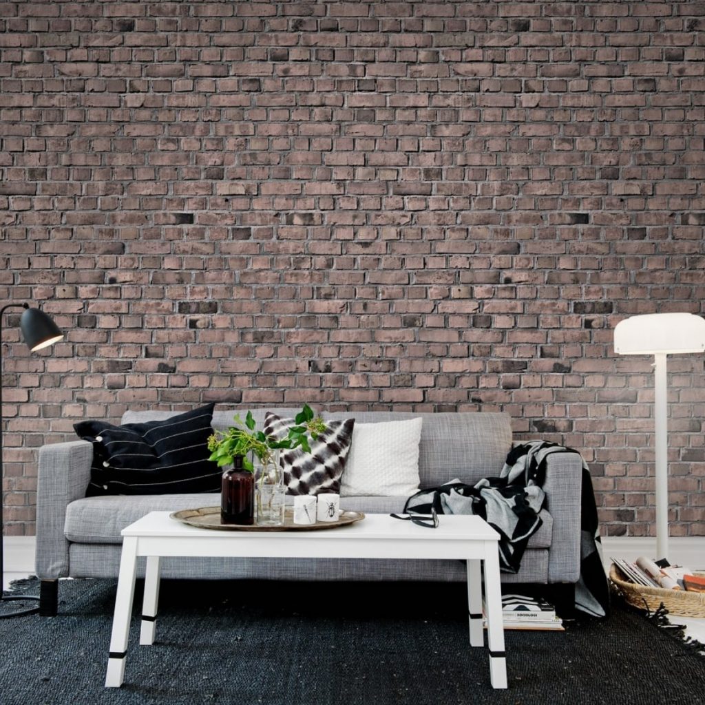 Fototapet 3D Brick Wall intr-un living cu canapea gri pe care se afla perne decorative si un pled, cu masuta de cafea alba pe care se afla o tava cu cani si vase cu plante