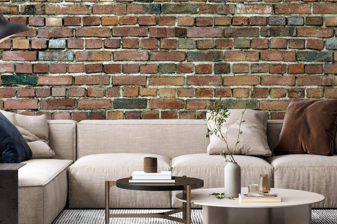 Fototapet Stockholm Brick Wall, personalizat, Photowall, intr-un living cu canapea bej si perne decorative si doua mese de cafea rotunde pe care se afla carti, planta decorativa