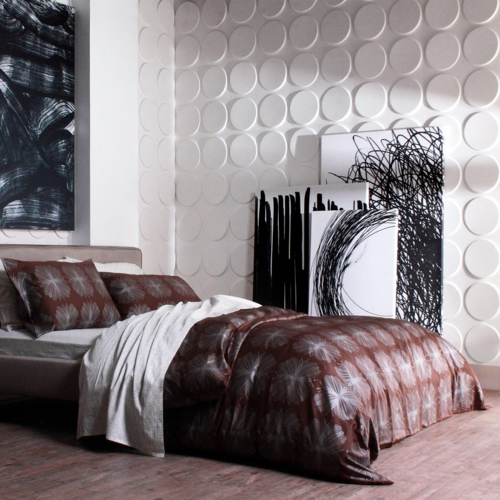 Panouri decorative 3D Ellipses, WallArt, de care sunt sprijinite trei tablori cu model abstract in alb si negru, intr-un dormitor cu pat