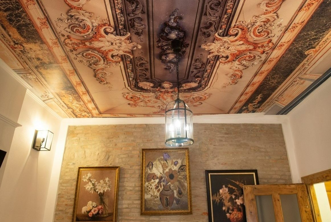 Incapere in stil neoclasic, cu fototapet pe tavan, candelabru, perete accent cu caramida aparenta si trei tablouri, usa din lemn si o aplica de perete
