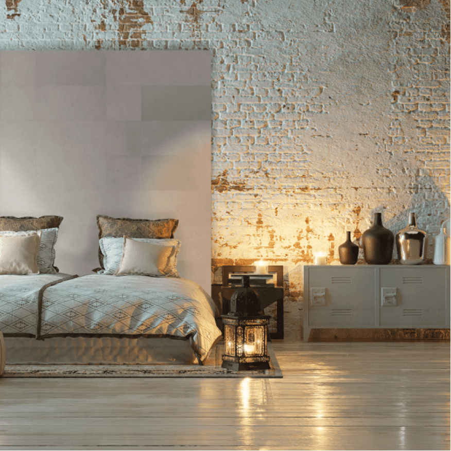 Tapet din piele naturala, Frost, Enzo Pellini, intr-un dormitor cu perete din caramida, pat, comoda cu vase decorative si o lampa aprinsa asezata pe covor