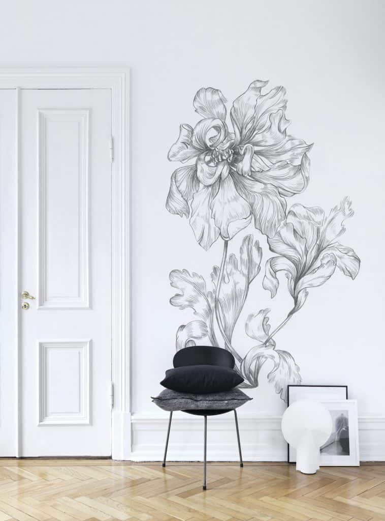 Tapet Peony pe un perete cu usa alba, in fata caruia se afla un scaun negru cu doua perne si doua tablouri sprijinite de podea