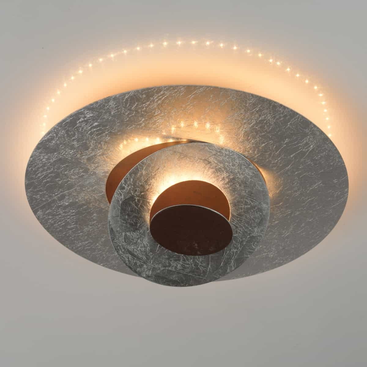 Lustra moderna hi-tech argintie, de la Demarkt, cu LED, cu lumina calda, in tonuri de oranj, pe un fundal gri deschis