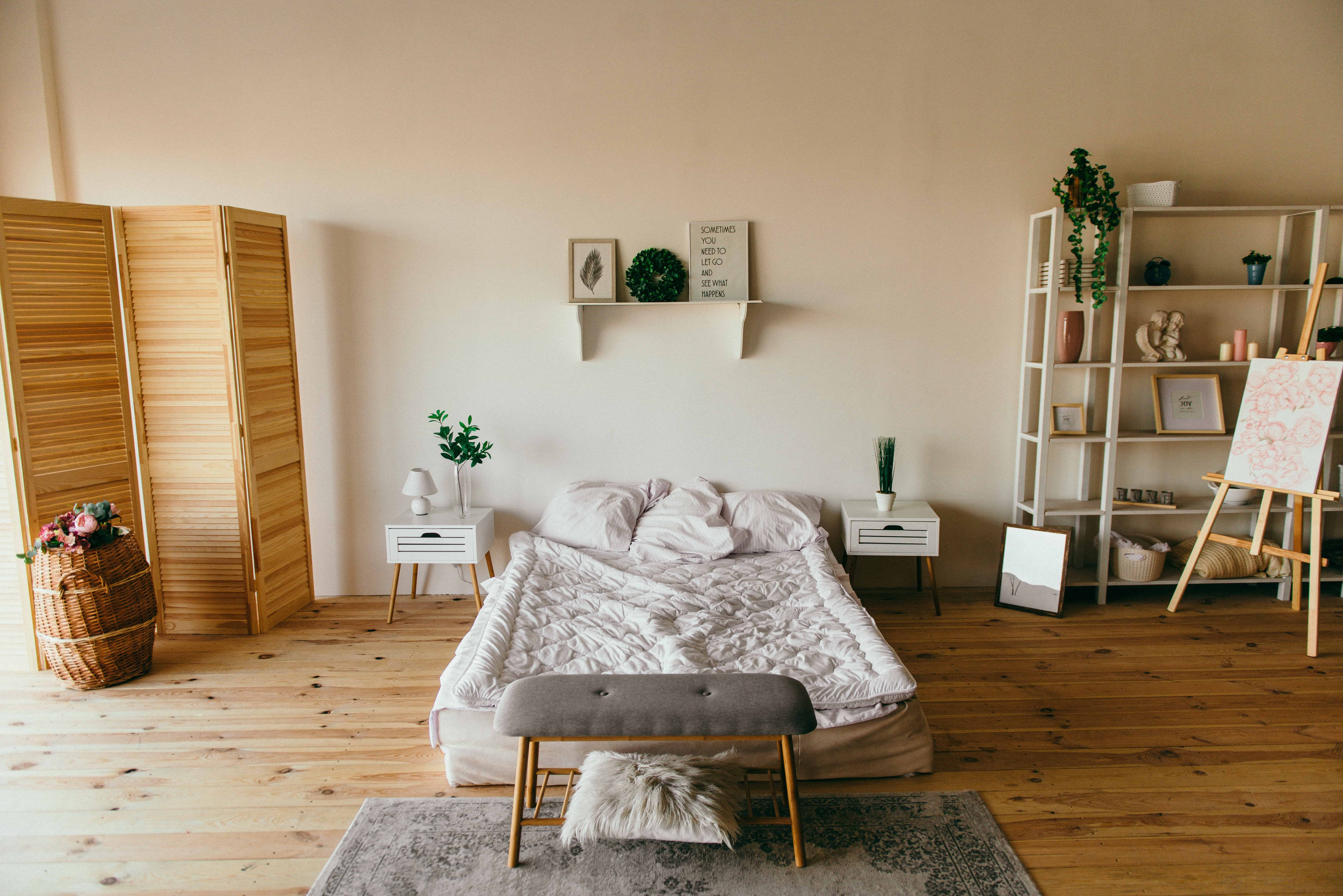 dormitor cu pereti bej, pat dublu cu lenjerie alba, podea si elemente de decor maro