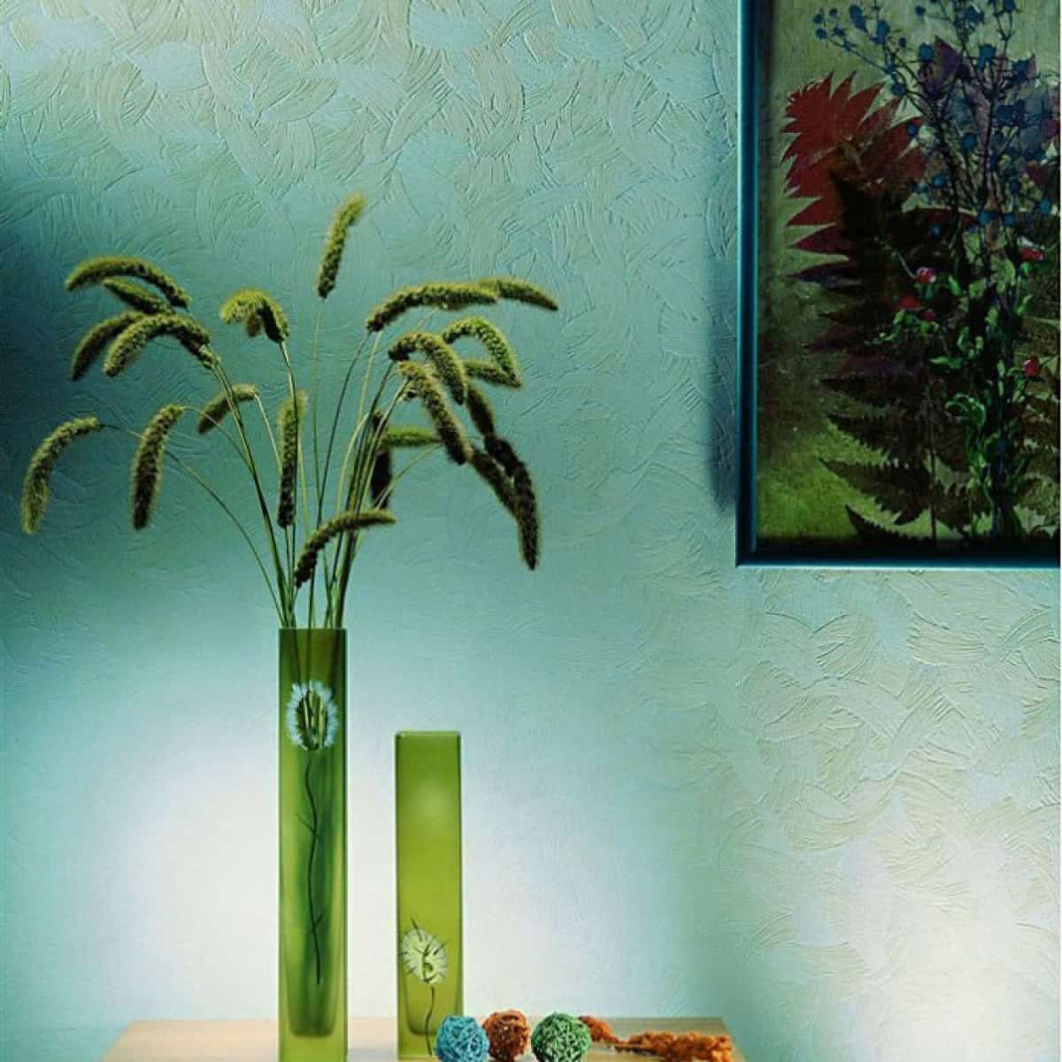 masa din lemn cu doua glastre de flori și alte decorațiuni, lipită de un perte cu tapet albastru pe care este atasat un tablou floral cu rama neagră