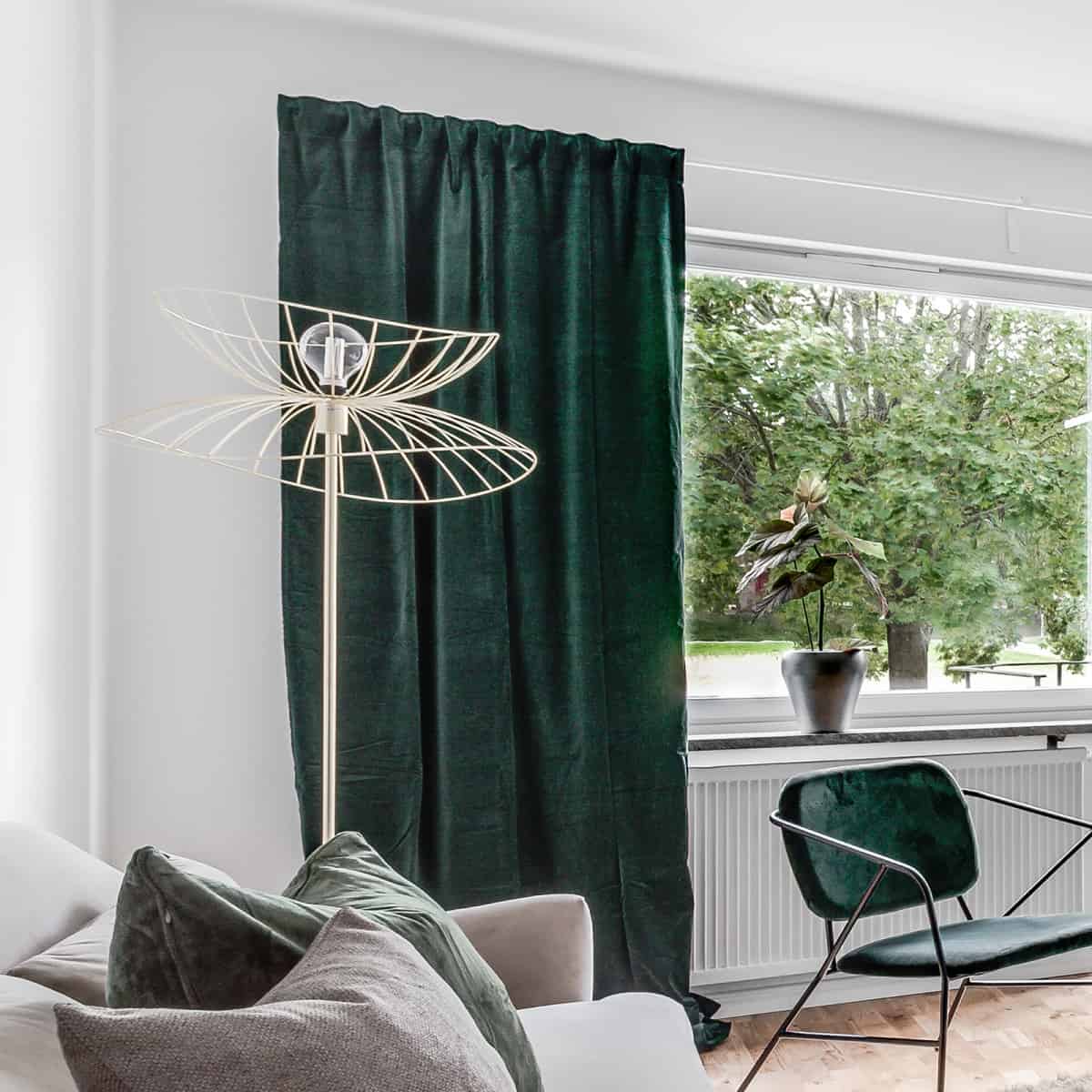 camera cu draperii verzi si lampadar din metal auriu cu picior si forme unduite pe marginea exterioara