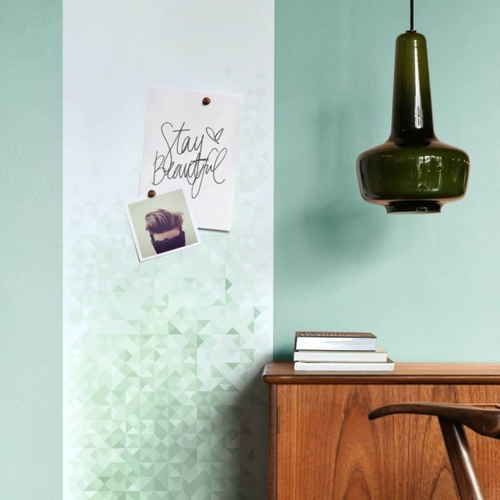 Tapet magnetic geometric verde cu doua fotografii, langa un birou din lemn pe care sunt asezate carti si un corp de iluminat suspendat