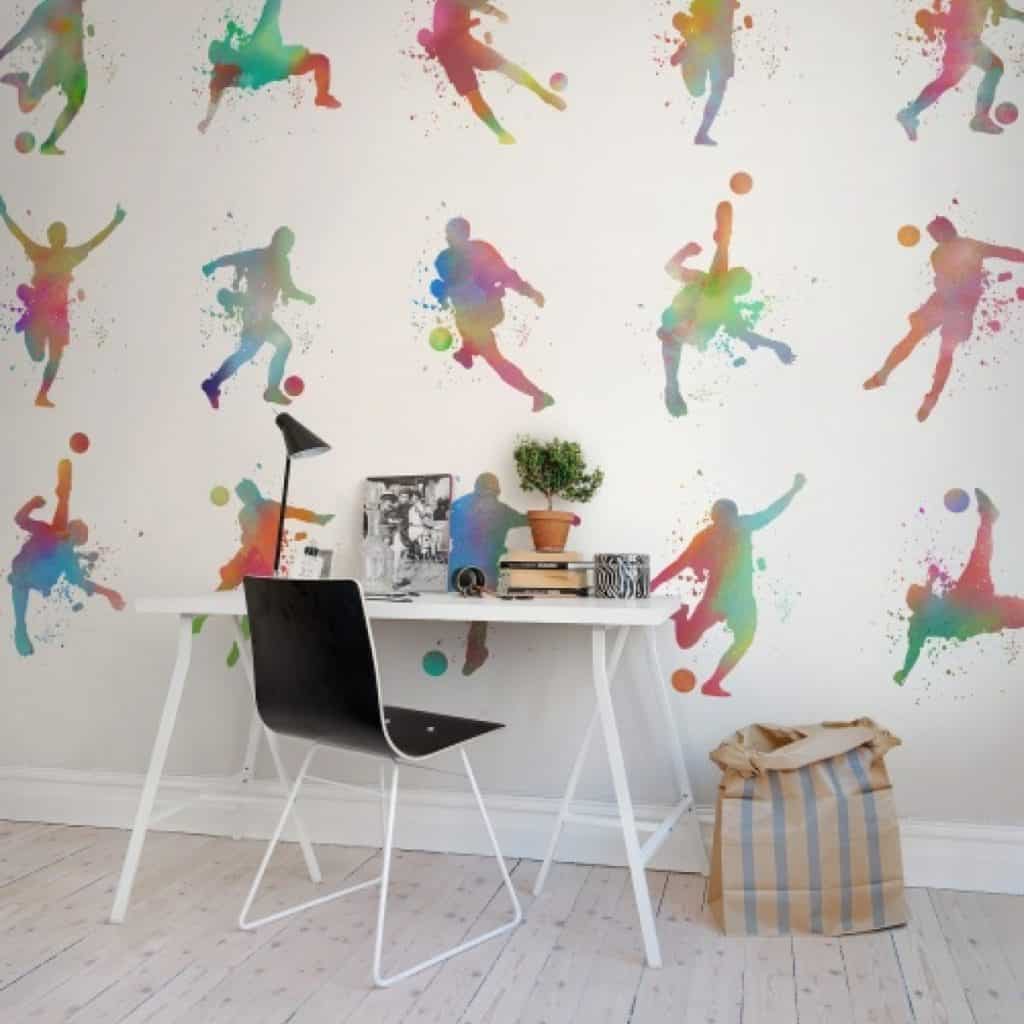 Perete decorat cu fototapet cu motive multicolore inspirate din sport, in fata caruia se afla o masa si un scaun