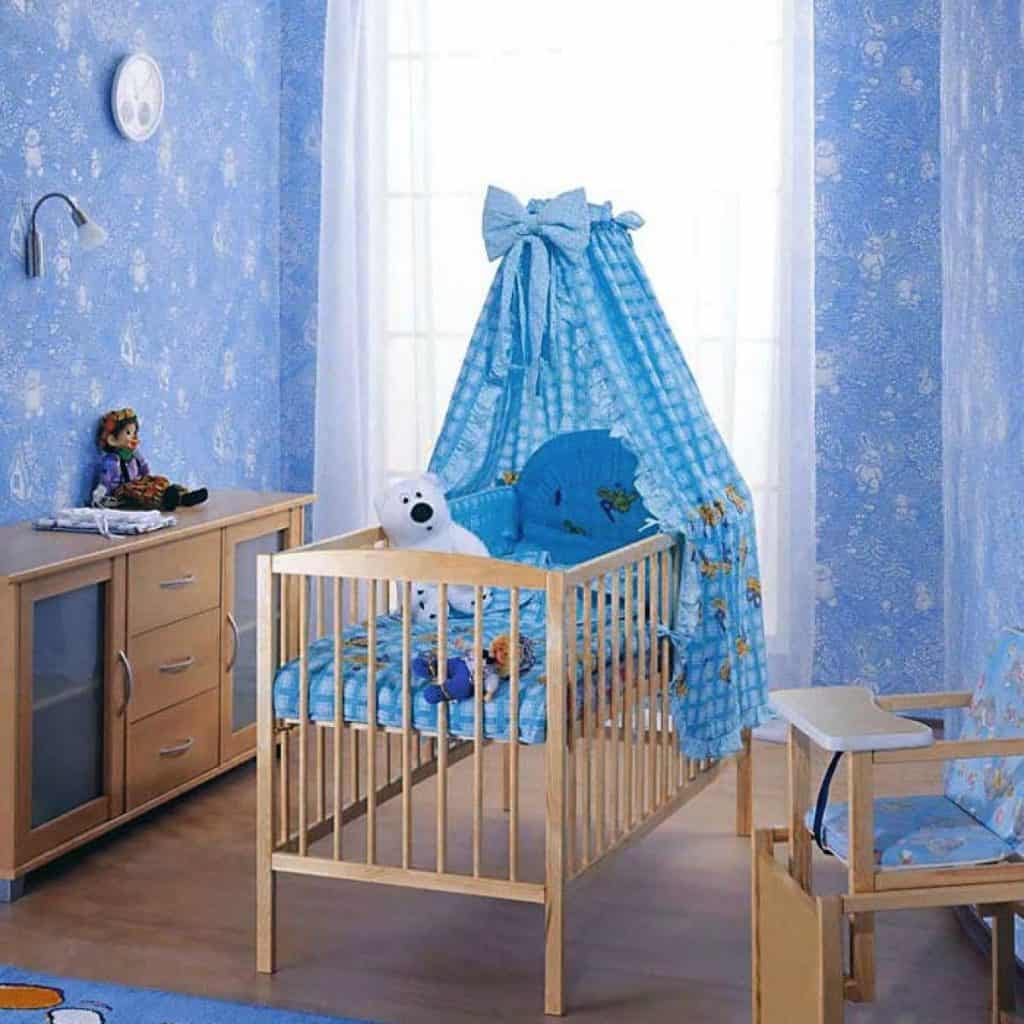 Camera bebelus cu pereti albastri, in mijloc cu un patut pentru copii și elemente de mobilier pe laterale