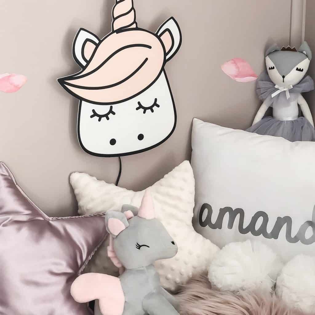 Aplica de perete Unicorn deasupra unui pat cu perne decorative si jucarii din plus