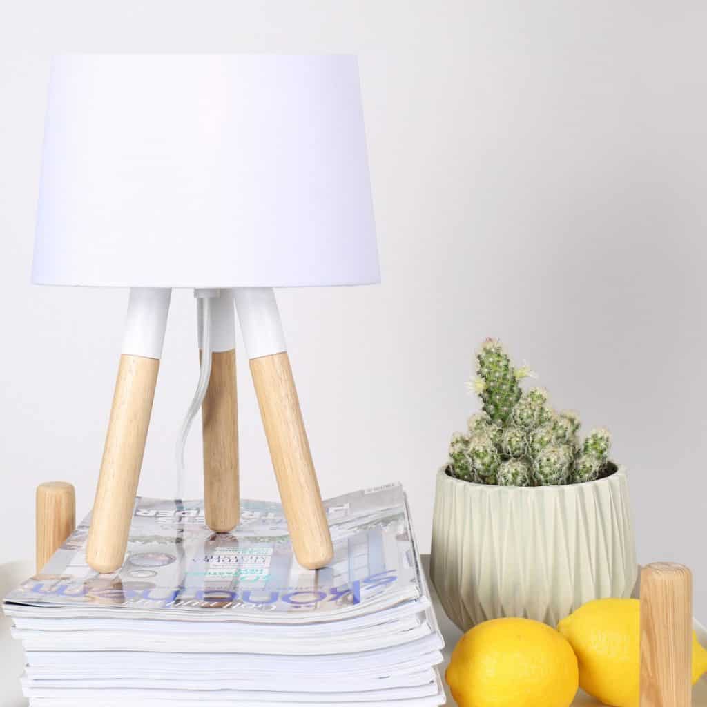 Lampa de birou alba, asezata pe un teanc de reviste, langa un vas cu un cactus si doua lamai