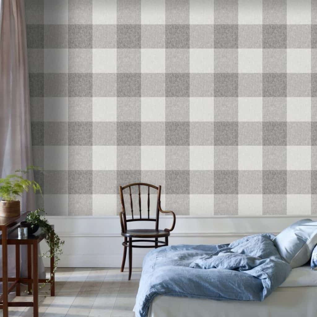 Perete cu tapet in carouri alb si gri, intr-un dormitor cu pat, scaun negru si comoda cu plante decorative