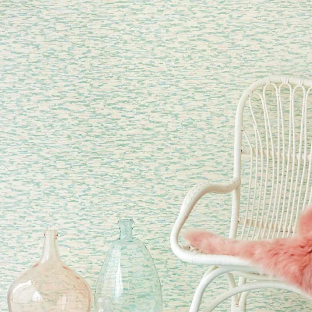 Perete cu tapet in nuante de albastru, verde si alb, in fata caruia se afla un fotoliu alb cu blana roz si doua vase decorative