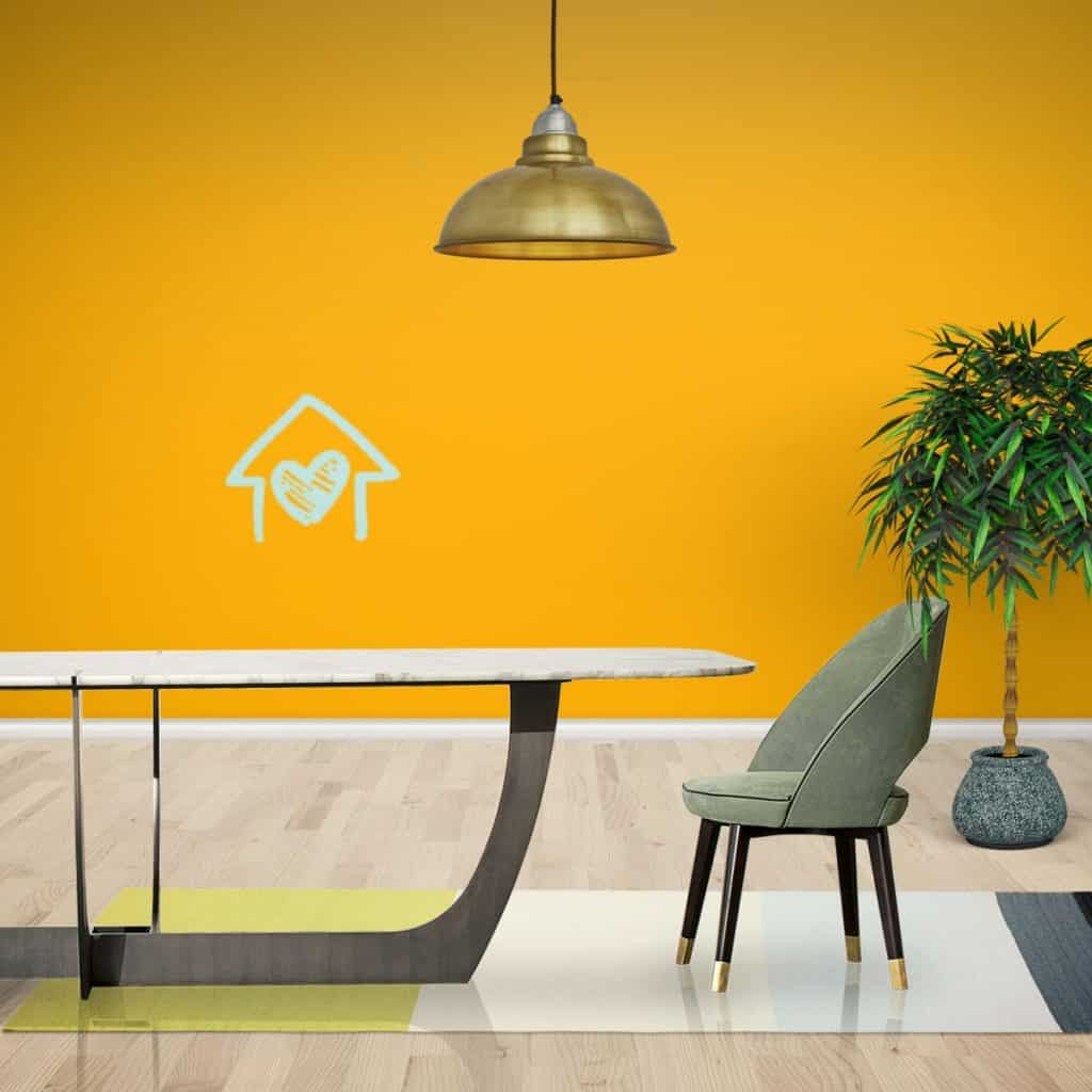 Perete decorat cu vopsea lavabilă galbena intr-o camera cu masa si fotoliu gri si o planta decorativa