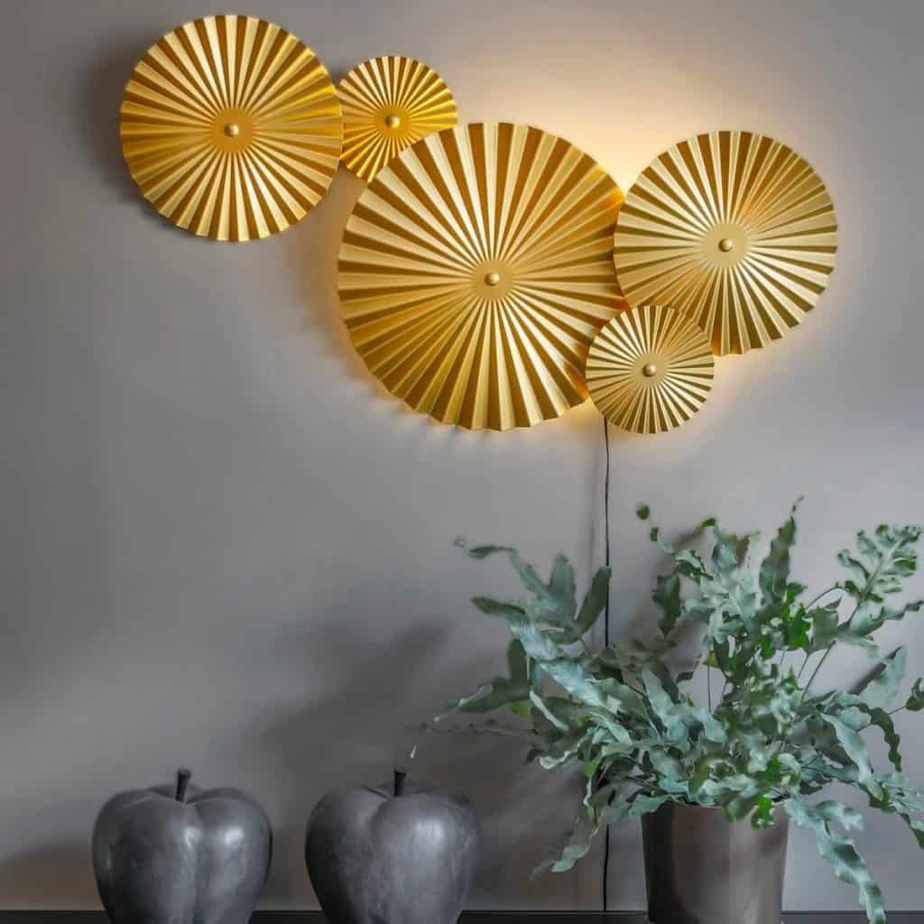 Aplica de perete Omega cu 5 cercuri galbene pe un perete gri, langa care se afla o planta si doua obiecte decorative in forma de mar