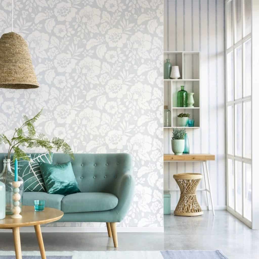 Tapet Blend Eijffinger alb si albastru deschis intr-un living cu canapea albastra, masa, rafturi si obiecte decorative din sticla verde si turcoaz