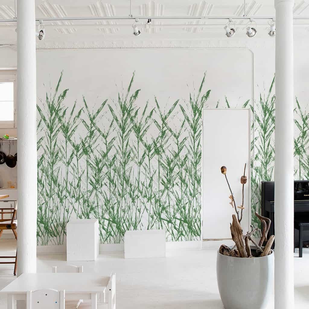 Perete cu tapet Rosseau Trestintas, alb cu trestii verzi, intr-o incapere cu vas decorativ alb cu o planta, coloane albe si elemente de mobilier negru si alb