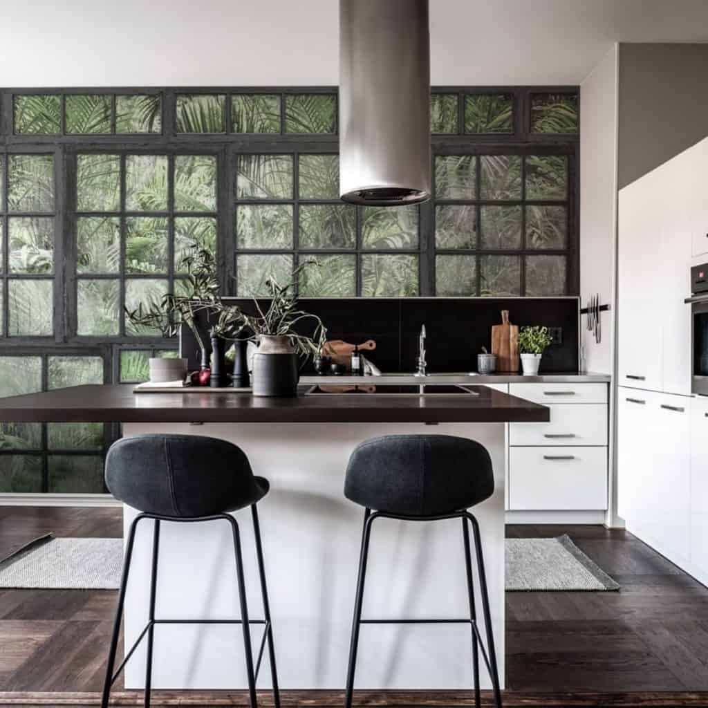 Fototapet Perspective Jardin Noir intr-o bucatarie cu mobilier alb si blaturi negre, cu insula, doua scaune negre, hota si plante decorative