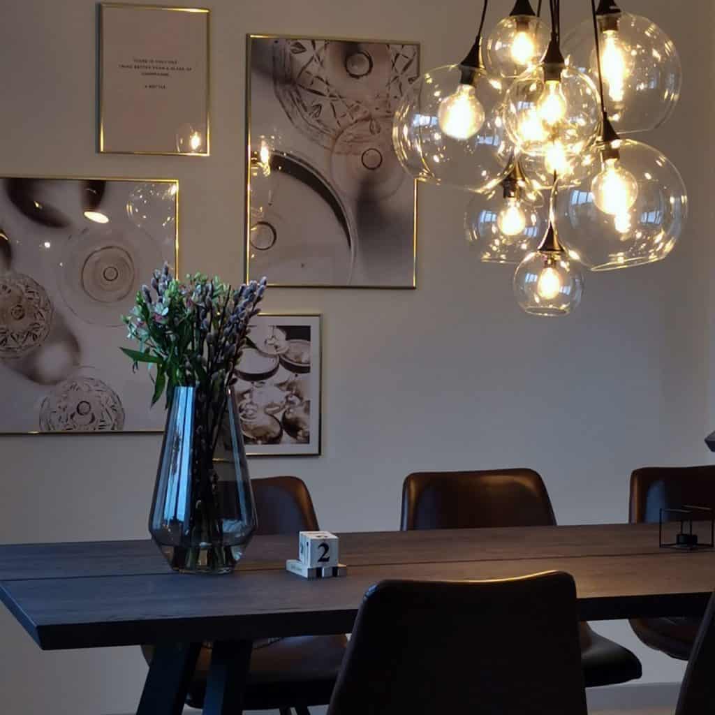 Lustra Pallas cu 9 globuri din sticla de diferite dimensiuni intr-o incapere cu trei tablouri, masa neagra pe care se afla o vaza cu flori si un obiect decorativ si scaune