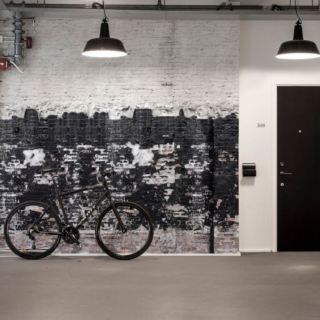 Fototapet 3D Domino, Rebel Walls, in fata caruia se afla o bicicleta neagra, intr-o incapere cu usa neagra si doua corpuri de iluminat suspendate