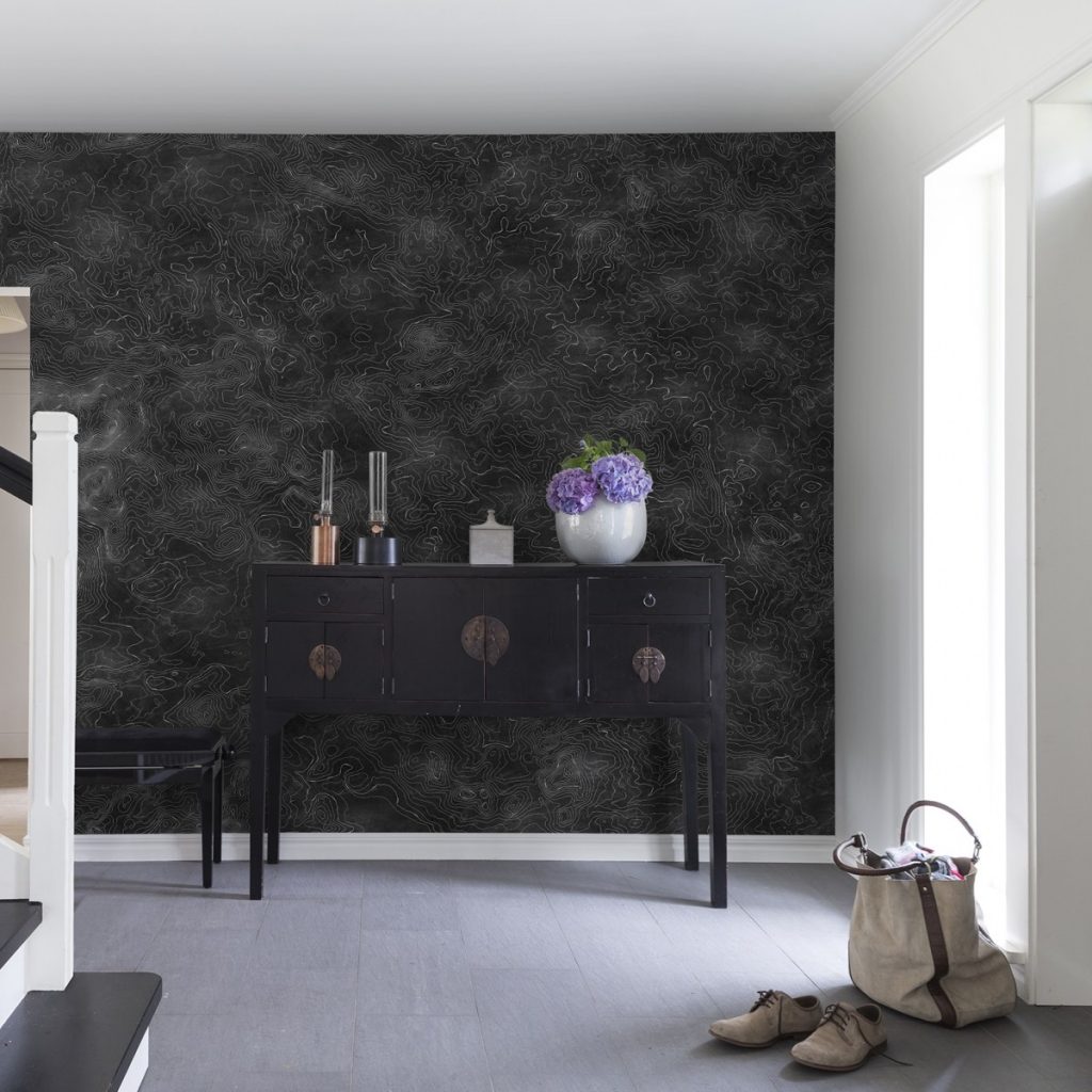 Fototapet Elevation Lines, Negru, personalizat, Rebel Walls, intr-o incapere cu comoda neagra pe care se afla un vas alb cu flori si obiecte decorative, o geanta si o pereche de ghete
