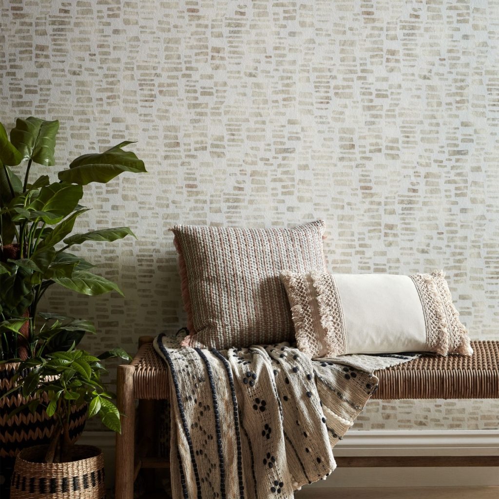 Tapet bej Fusion, 1838 Wallcoverings, intr-o incapere cu banca pe care se afla perne decorative, un pled si doua vase cu flori decorative