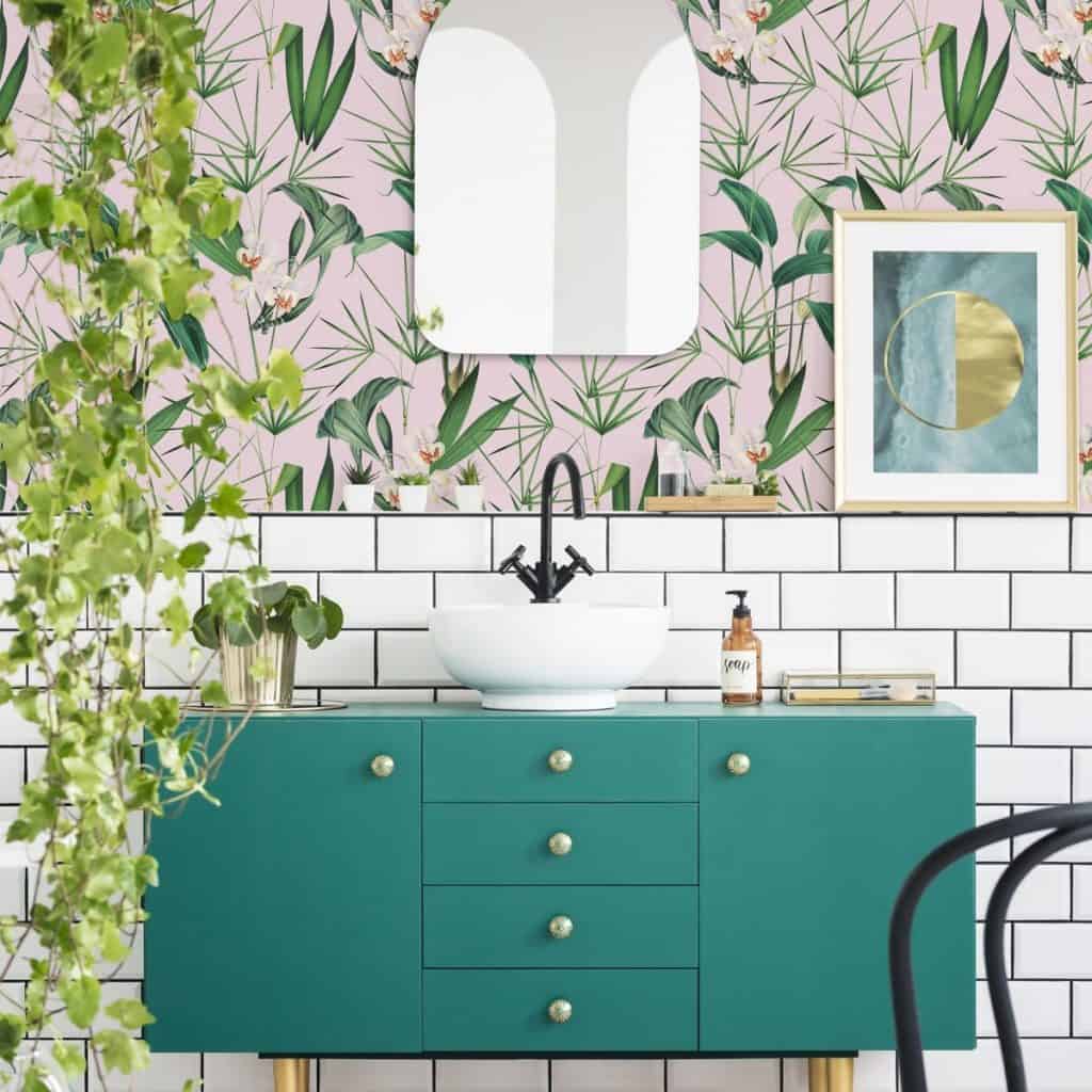 Tapet Palm Springs de la Mindthegap intr-o baie cu dulap verde pe care se afla lavoarul si articole de igiena, tablou, oglinda si planta decorativa