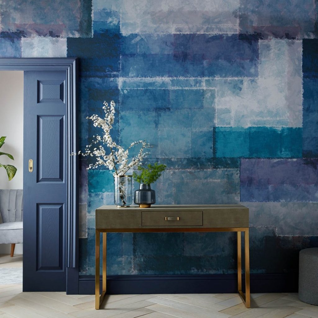 Tapet albastru Spectrum, 1838 Wallcoverings intr-o incapere cu usa albastra si comoda pe care se afla doua vase cu flori