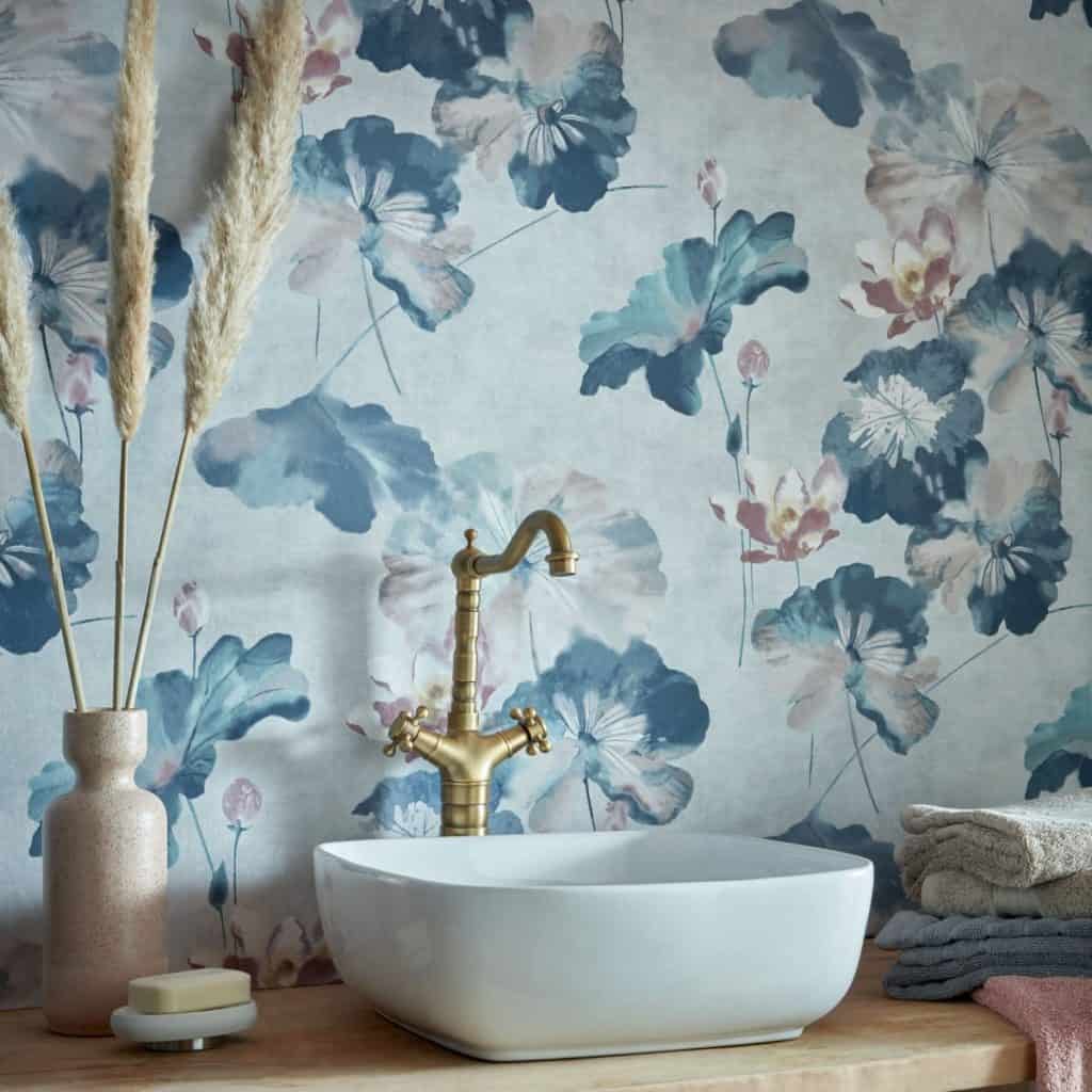 Tapet Water Lilies de la 1838 Wallcoverings intr-o baie cu lavoar alb si robinet auriu, langa care se afla prosoape, un vas cu palnta decorativa si sapun