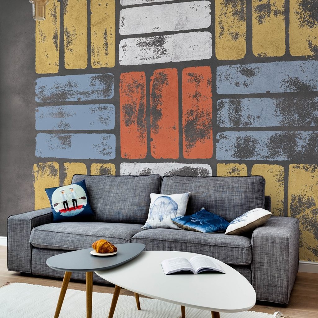 Fototapet Argile M2505-2, TresTintas, intr-un living cu canapea gri si perne decorative si masa de cafea compusa din doua elemente, alb si gri, pe care se afla o carte deschisa si o farfurie cu un croissant
