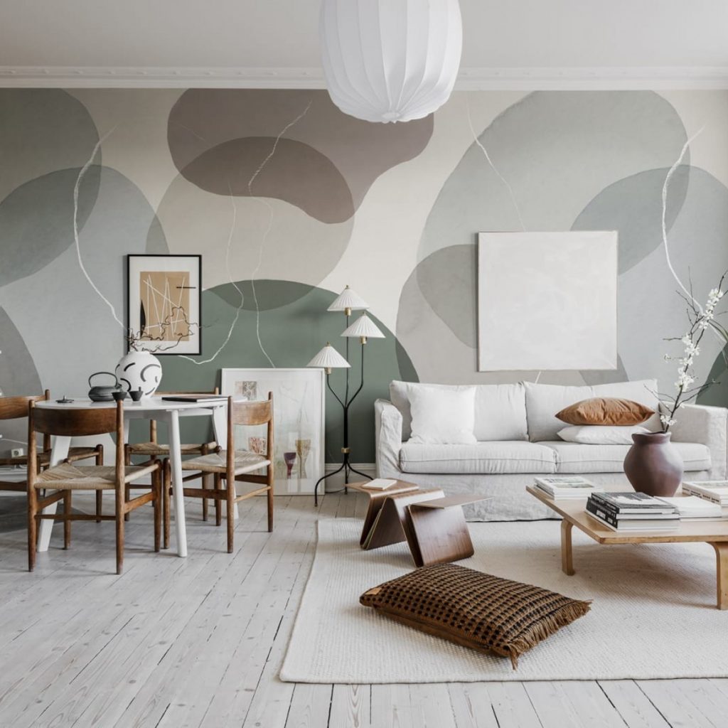 Fototapet Floating, Soft, Rebel Walls, intr-un living cu canapea alba si perne decorative, masa de cafea patrata din lemn pe care se afla carti si un vas cu floare, perna mare maro pe covorul alb, suport de reviste, masa rotunda alba cu scaune, tablouri si o lampa de podea