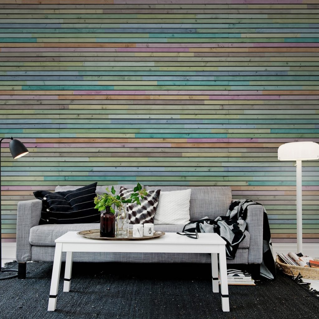 Fototapet Scanduri colorate, Rebel Walls, intr-un living cu canapea gri si perne decorative, covor negru, masa de cafea alba pe care se afla o tava cu cani si vase cu plante, doua lampi de podea si un cos cu reviste