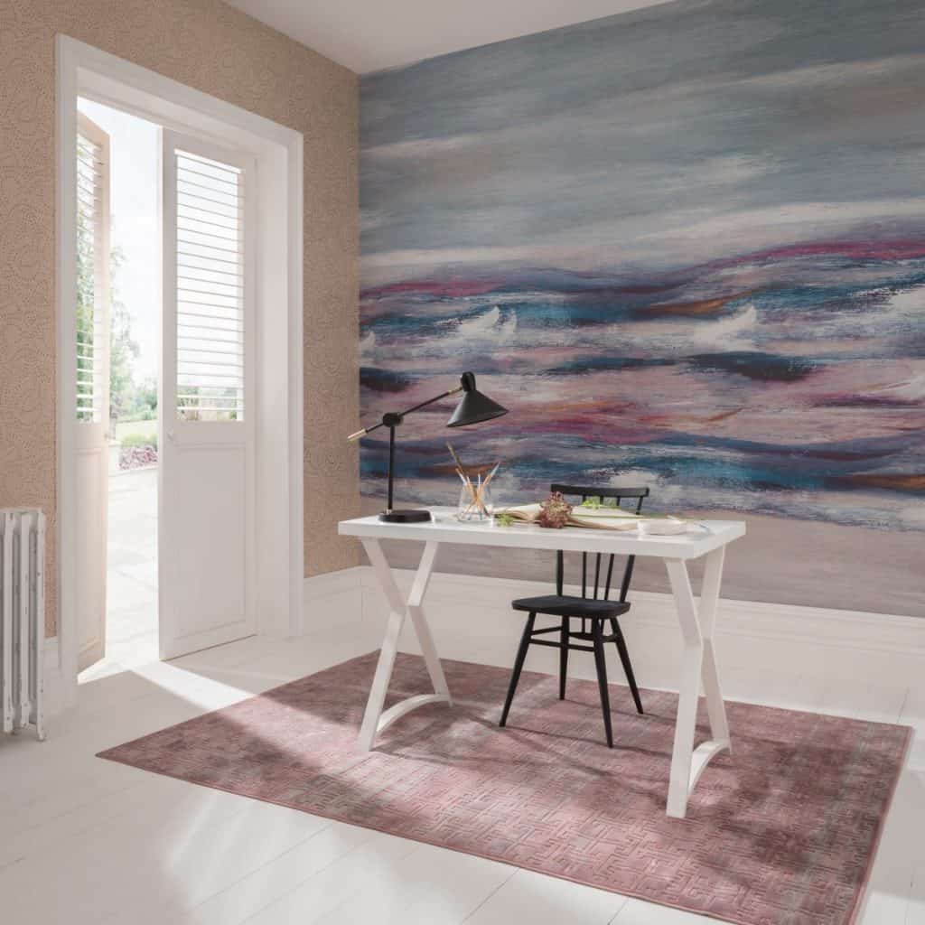 Tapet Bellavista, 1838 Wallcoverings, intr-o incapere cu usa alba, masa alba pe care se afla o lampa neagra si mai multe obiecte, scaun negru si covor roz nisipiu