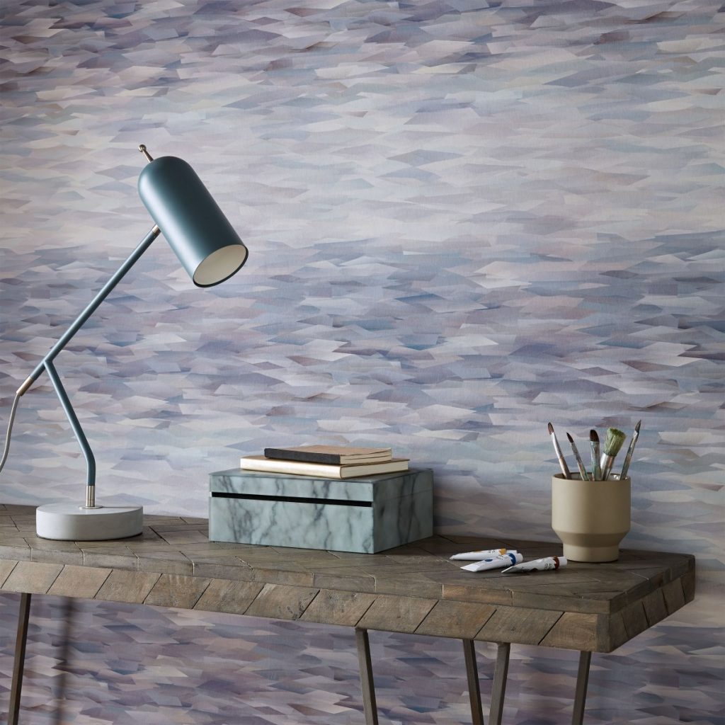 Tapet Prism, 1838 Wallcoverings, intr-o incapere cu masa cu lampa, pahar cu pensule, tuburi cu acuarela si o cutie pe care se afla doua carti