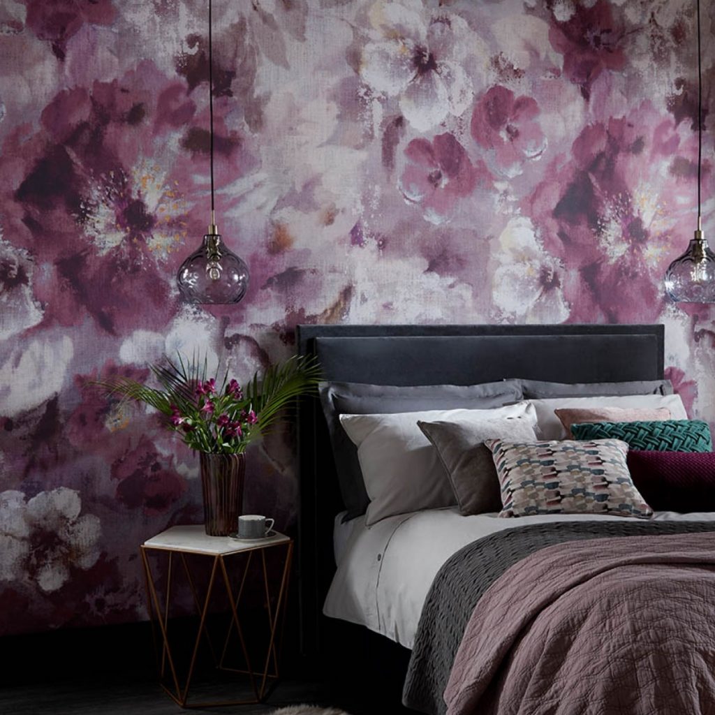 Tapet Bloom, 1838 Wallcoverings, intr-un dormitor cu pat pe care se afla perne decorative colorate, doua corpuri de iluminat suspendate si masuta cu cana de cafea si vas cu flori